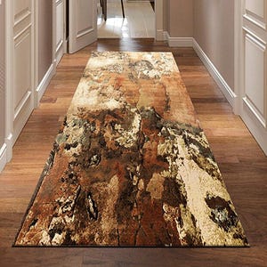 Puede incluir: Una alfombra rectangular para pasillo con un diseño desgastado y texturizado. La alfombra presenta una paleta de colores de marrones, beiges y verdes, creando una apariencia rústica y envejecida. La alfombra está colocada sobre un suelo de madera.