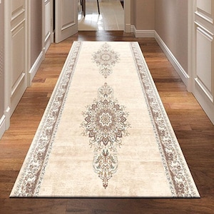 May include: A beige hallway runner rug with an intricate floral and geometric pattern in shades of brown, cream, and gold. The rug is rectangular and placed on a wooden floor, adding warmth and style to the space.