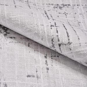 May include: Close-up of a textured, light gray fabric with a subtle grid pattern and dark gray, abstract markings. The fabric is folded, revealing its layered texture and design. Ideal for home decor or textile projects.