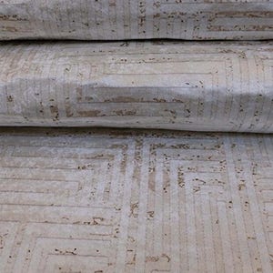 Puede incluir: Alfombra beige enrollada con un patrón geométrico. El diseño presenta una serie de cuadrados y líneas interconectados en un beige más claro, creando una apariencia texturizada. La alfombra tiene un aspecto suave y afelpado.