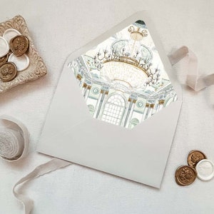 May include: A white envelope with a gold and green illustration of a chandelier and a room with columns. The envelope is on a white surface with gold and white wax seals.