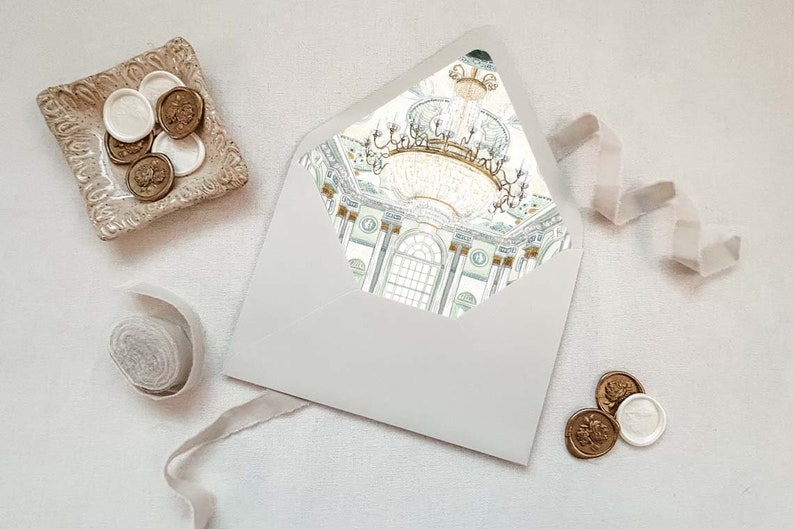 May include: A white envelope with a gold and green illustration of a chandelier and a room with columns. The envelope is on a white surface with gold and white wax seals.