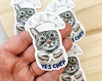 May include: Four white stickers with a cartoon illustration of a gray tabby cat wearing a white chef's hat. The cat is looking directly at the viewer. The text "YES CHEF" is printed in blue on the sticker.