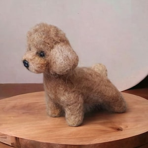 May include: A brown needle felted poodle dog figurine. The poodle is sitting on a wooden surface.