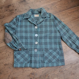 Può includere: Una giacca blu e bianca a quadri con una toppa sul gomito e due tasche. La giacca ha una chiusura con bottoni.