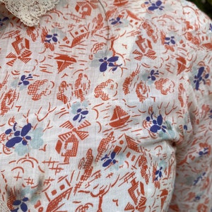 May include: White cotton fabric with a repeating pattern of orange houses, blue flowers, and sailboats. The fabric has a slightly textured surface.