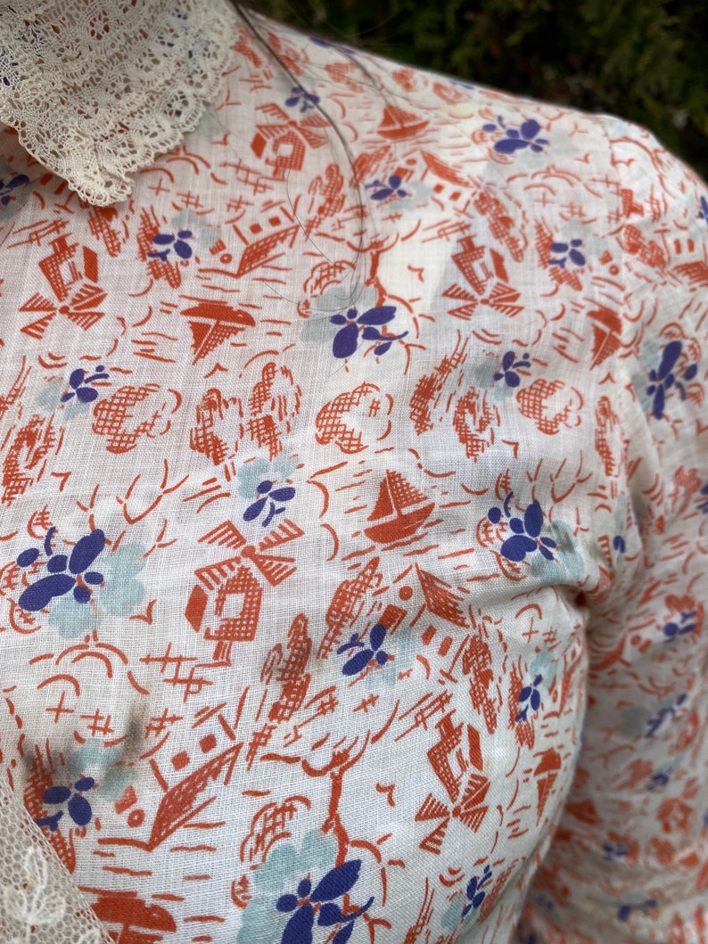 May include: White cotton fabric with a repeating pattern of orange houses, blue flowers, and sailboats. The fabric has a slightly textured surface.