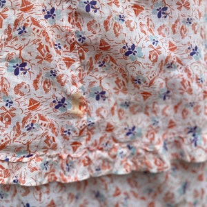 May include: White fabric with a repeating pattern of small orange houses, blue flowers, and sailboats. The fabric has a ruffled edge.