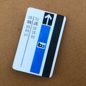 May include: A white rectangular card with a blue vertical stripe and a black stripe on the right side. The card features the text "19 72", "09 25", "05 10", "04 15", and "04 08". The card also has the logo "ba" and an upward-pointing arrow.