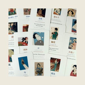 May include: A collection of rectangular white cards featuring various Japanese-inspired illustrations of people and nature. Each card displays a unique artwork, a Japanese word in kanji and romaji, and a short English definition or phrase.