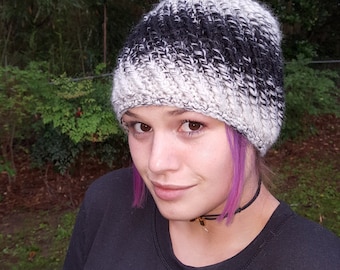 May include: A black and white knit beanie with a gradient pattern. The beanie is worn by a person with purple hair.
