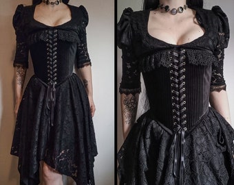 Op de afbeelding: Zwarte gothic jurk met een fluwelen corset met vetersluiting en een gelaagde kanten rok. De jurk heeft een bolero-top met kanten mouwen en een sweetheart halslijn. Het ontwerp is donker en elegant.