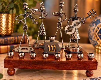 May include: A wooden menorah base with eight silver-toned metal candle cups, featuring four metal musician figurines and a central wooden dreidel with the Hebrew letter Shin in gold. The base stands on four small wooden feet.