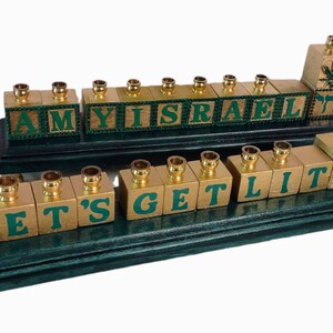 May include: A green and gold menorah with the words "AMY ISRAEL" and "LET'S GET LIT" spelled out on the candle holders. Each candle holder is a block with a green background and gold lettering. The menorah has a green wooden base.