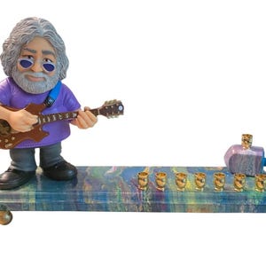 May include: A colorful menorah with a figurine of a man playing a guitar. The menorah has a marbled design with gold-colored candle holders. A dreidel is on the right side of the menorah.