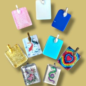 May include: Assortment of eight rectangular glass pendants with various designs and colors. The pendants feature a gold, silver, or white metal bail. Designs include a pink glitter, a white solid color, a blue solid color, a gold glitter, a koi fish, a turquoise solid color, a tie-dye with a heart, and a dragon.