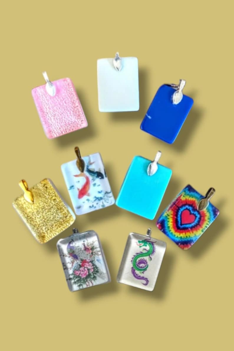 May include: Assortment of eight rectangular glass pendants with various designs and colors. The pendants feature a gold, silver, or white metal bail. Designs include a pink glitter, a white solid color, a blue solid color, a gold glitter, a koi fish, a turquoise solid color, a tie-dye with a heart, and a dragon.