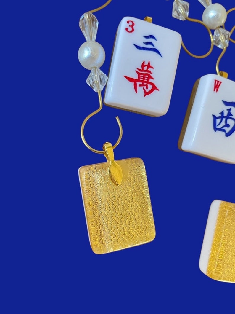 May include: Gold pendant earrings with a textured gold surface. The earrings are shaped like a square and have a small gold loop at the top. The earrings are hanging from a gold chain.