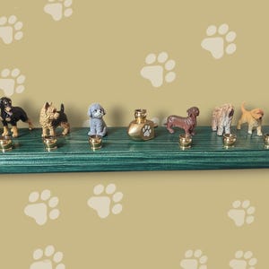 Könnte beinhalten: Ein grünes Holzregal mit Messinghaken hält eine Sammlung kleiner Hundefiguren. Das Regal hat ein Pfotenabdruckdesign und ist mit einer kleinen Flasche Hundefluid dekoriert.