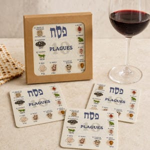 May include: A set of square coasters featuring the 10 Plagues of Egypt with Hebrew and English text, including illustrations of blood, frogs, lice, wild beasts, cattle disease, boils, hail, locusts, darkness, and death of firstborn, in a box.