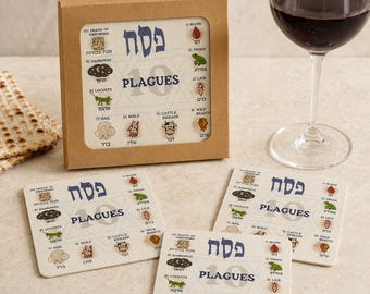 May include: A set of square coasters featuring the 10 Plagues of Egypt with Hebrew and English text, including illustrations of blood, frogs, lice, wild beasts, cattle disease, boils, hail, locusts, darkness, and death of firstborn, in a box.