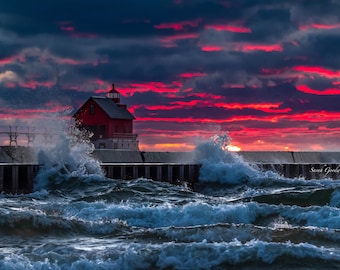 May include: A red lighthouse stands on a pier with crashing waves in the foreground. The sky is a vibrant red and purple with dark clouds.