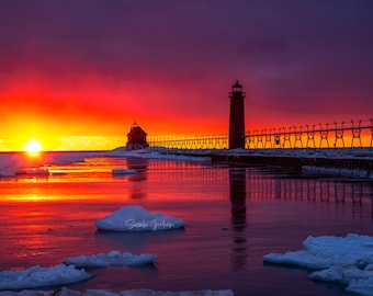 May include: A red and purple sunset over a frozen lake with a lighthouse and pier silhouetted against the sky.