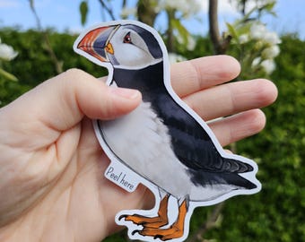 May include: A white and black puffin sticker with an orange beak. The sticker has a white background and the text "Peel here" is printed on the bottom.