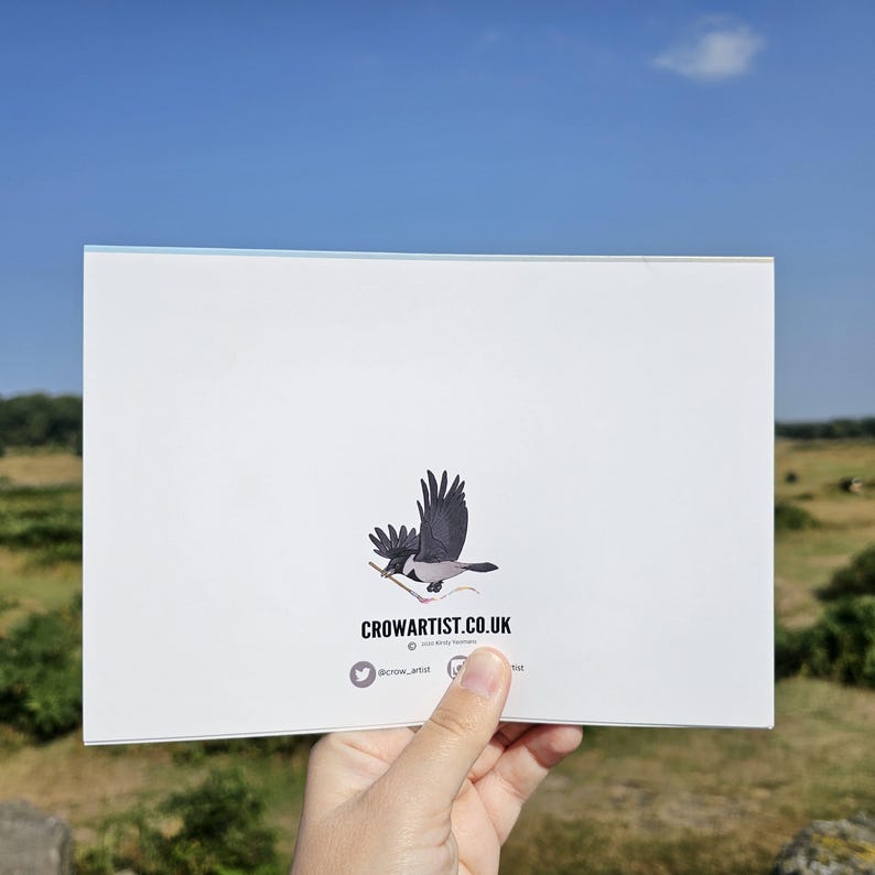 Puede incluir: Tarjeta blanca con una ilustraci&oacute;n de un cuervo negro y gris sosteniendo una ramita. La tarjeta muestra el texto "CROWARTIST.CO.UK" y detalles de redes sociales. El fondo muestra un cielo azul y un paisaje verde.