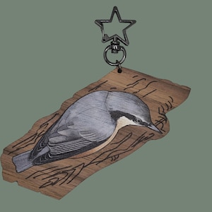 May include: A wooden keyring with a detailed illustration of a bird, possibly a nuthatch, with grey and white feathers, set against a wood-grain background. The keyring has a star-shaped clasp.