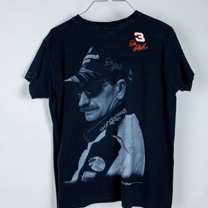 May include: Black t-shirt with a faded image of a race car driver wearing sunglasses and a cap. The shirt has the number "3" and the text "Dale Earnhardt Jr." printed on the back.