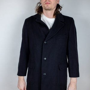 Peut inclure: Un long manteau noir à manches longues avec une fermeture à boutons et deux poches à rabat. Le manteau est fait d'un tissu épais et texturé.