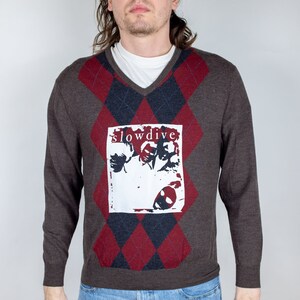 May include: A brown sweater with a red and black argyle pattern. The sweater has a white graphic of a band called "Slowdive" on the front.