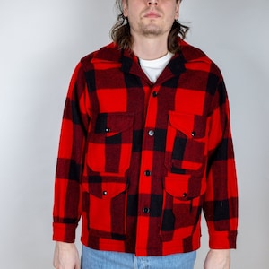 May include: A man wearing a red and black checked flannel shirt with a green and white baseball cap that says "Miller High Life" on the front. He is also wearing blue jeans.