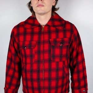 May include: A red and black plaid flannel jacket with a zipper closure. The jacket has two flap pockets on the chest and a buttoned cuff on the left sleeve.