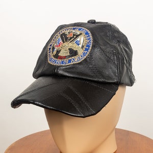 May include: Black leather baseball cap with a stitched design. The cap features a circular emblem with the words "DEPARTMENT OF THE ARMY" and "UNITED STATES OF AMERICA" in a blue border. The emblem also includes an eagle and flags.