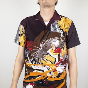 Puede incluir: Una camisa de manga corta con botones y un estampado colorido de inspiración anime con un guerrero samurái y un dragón. La camisa es negra con detalles en marrón, amarillo, rojo y blanco.