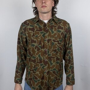 May include: A long-sleeved button-up shirt with a camouflage pattern in shades of green, brown, and tan.