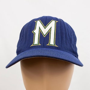 May include: A navy blue baseball cap with a white "M" embroidered on the front. The "M" has a green outline.