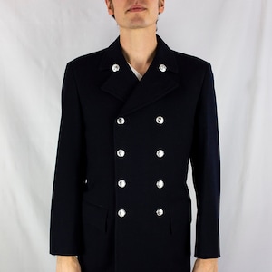 Pode incluir: Um blazer azul marinho de botões duplos com botões prateados. O blazer tem um colarinho de entalhe e dois bolsos de aba.