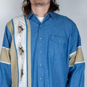 May include: A blue denim long-sleeve shirt with a tan, white, and blue striped panel down the front. The panel features embroidered horse heads. The shirt has a button-down front and a pointed collar.