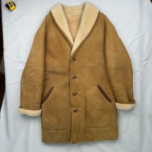 Könnte beinhalten: Ein beigefarbener Wildledermantel mit cremefarbenem Shearling-Futter und -Kragen. Der Mantel hat eine Knopfleiste, zwei Vordertaschen mit braunen Zierleisten und Shearling-Manschetten. Dieser Vintage-Mantel ist ein klassisches Oberbekleidungsstück.