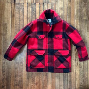 May include: A red and black checked wool jacket with a large collar and four front pockets. The jacket has a button-up closure and is made of a thick, warm material, suitable for cold weather.