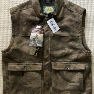 May include: A camouflage-patterned vest with two front pockets and a collar. The vest has a tag that reads "Cabela's" and "Outfitter". The vest is brown, green, and tan.
