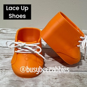 May include: A pair of bright orange shoes with white laces and a lace-up design. The text "Lace Up Shoes" appears in a black box at the top left, and the text "@busybeecabbies" is printed in white across the bottom of the orange shoes.