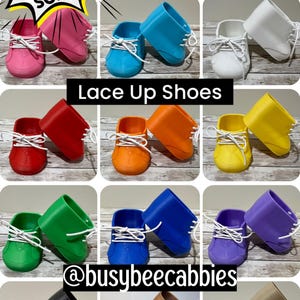 May include: A collection of lace-up shoes for Cabbage Patch Kids dolls in various solid colours including pink, blue, white, red, orange, yellow, green, purple, black, brown, and tan. Each shoe features white laces and a textured toe detail.