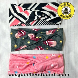 May include: Three colorful fabric headbands with a knotted design. The top headband has a black and white geometric pattern with pink accents. The middle headband has a gray background with pink and white tongue-shaped designs and yellow stars. The bottom headband has a pink background with a white and yellow cartoon character design and pink stars. The text "Busy Bee Headbands" is visible in the top right corner of the image.