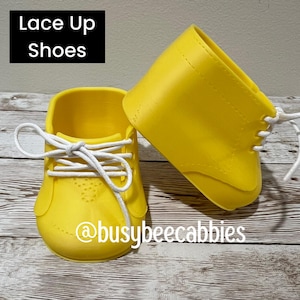 May include: A pair of bright yellow shoes with white laces and the text Lace Up Shoes and @busybeecabbies visible. The shoes feature a smooth, moulded construction with a rounded toe and a high-top design, showcasing a clean, solid colour finish.