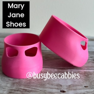 May include: Two bright pink, cup-shaped silicone sleeves featuring two side cutouts each. The text "Mary Jane Shoes" appears in the top left corner, and the text "@busybeecabbies" is printed in white at the bottom center of the image.