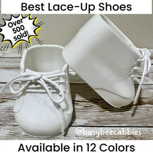 May include: Two white lace-up shoes with white laces. The text reads Best Lace-Up Shoes, Over 500 sold!, and Available in 12 Colors. The handle @busybeecabbies is also visible. The shoes have a smooth finish and a classic ankle-high design.